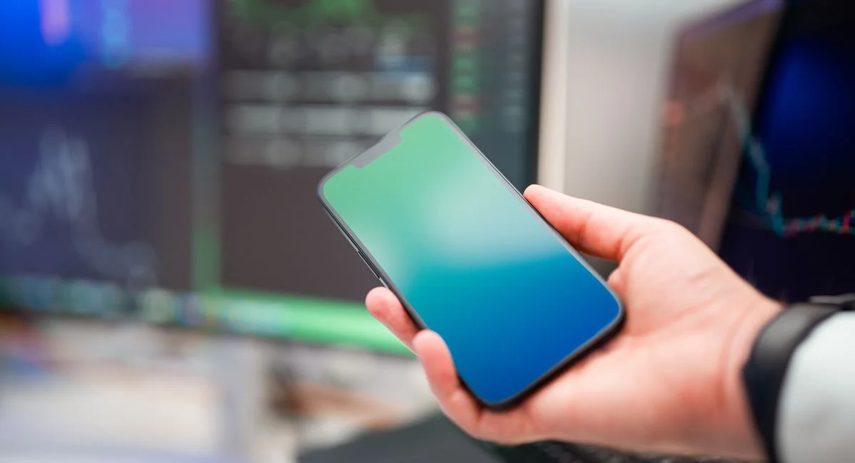 Main posant un smartphone sur un bureau avec une application bancaire ouverte montrant un virement d'épargne