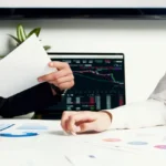 Main tenant un relevé bancaire imprimé devant un ordinateur ouvert