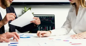 Main tenant un relevé bancaire imprimé devant un ordinateur ouvert