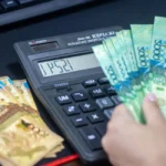 Salarié consultant sa fiche de paie avec calculatrice et ordinateur ouvert