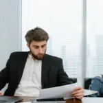 Un homme lit un relevé bancaire, calculatrice sur la table, ambiance matinale