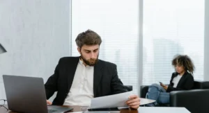 Un homme lit un relevé bancaire, calculatrice sur la table, ambiance matinale